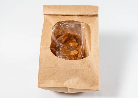 Brown paper bag with a clear window containing caramel chews on a white background