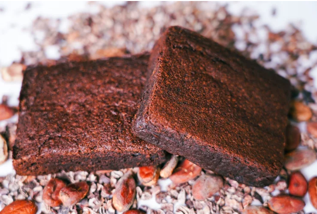 Two pieces of dark chocolate brownie on a bed of cacao nibs and cocoa powder.