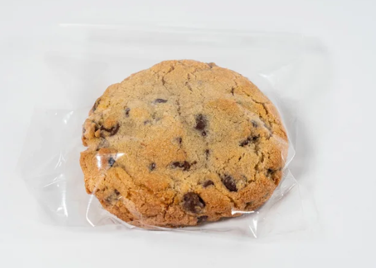 Chocolate chip cookie in clear plastic wrap on a white background