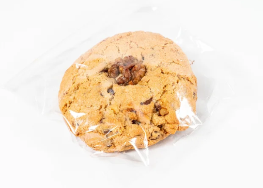 Chocolate chip cookie with walnuts wrapped in plastic on a white background