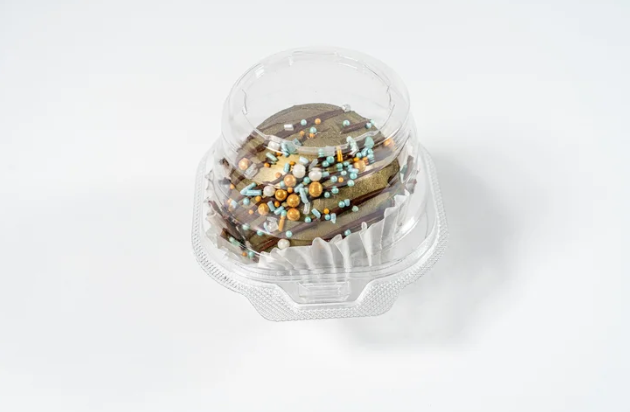 Small cocoa bomb with decorative sprinkles in a clear plastic container on a white background