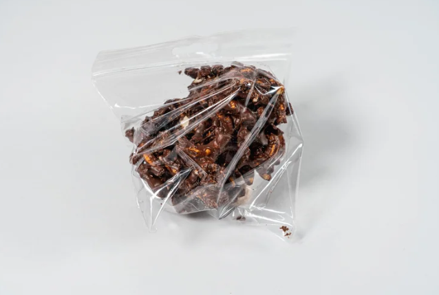 Clear plastic bag with chocolate nut pretzel clusters on a white background