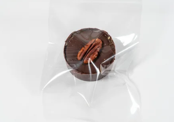 Chocolate-covered pecan caramel turtle in clear plastic packaging on a white background