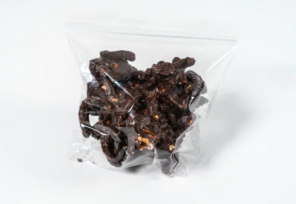 Clear plastic bag filled with dark chocolate pretzel nut clusters on a white background