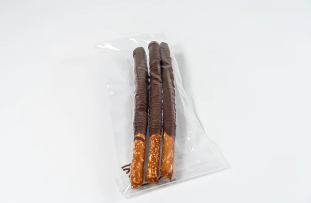 Three chocolate-dipped pretzel rods in a clear plastic bag on a white background