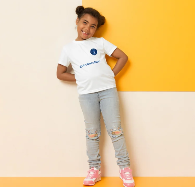 Child wearing a white t-shirt with text and gray jeans against a yellow and beige background