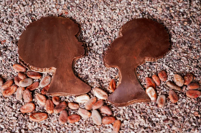 Two chocolate cookies shaped like black women on a bed of cacao beans