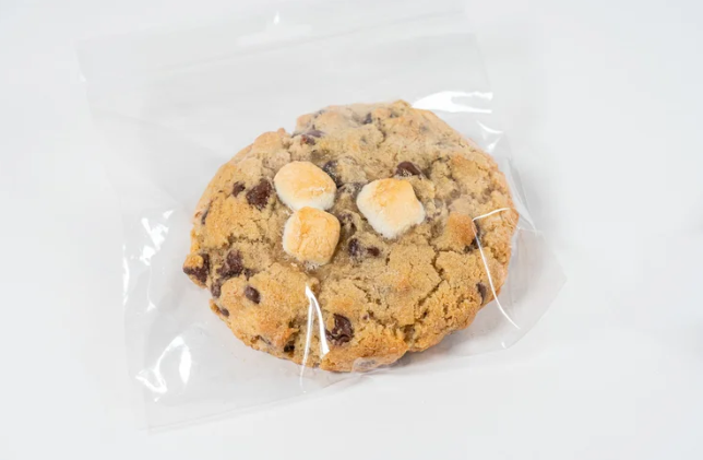 Chocolate chip cookie with marshmallows in clear plastic wrap on a white background
